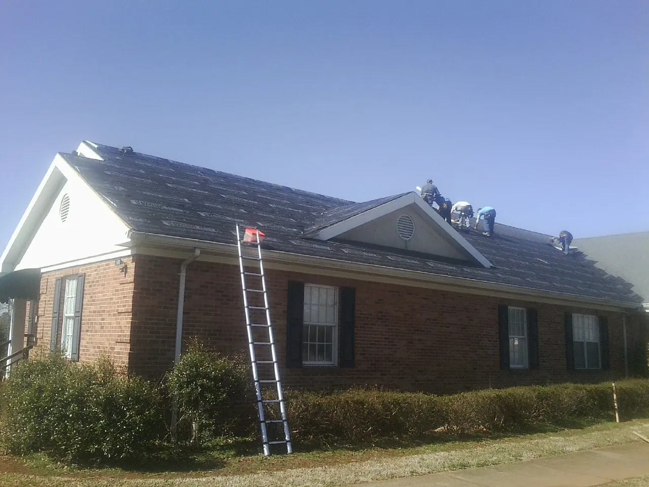 Crew tearing shingles off a brick ranch roof with a ladder set — Emergency Roof Repair work by our crew in Woodland